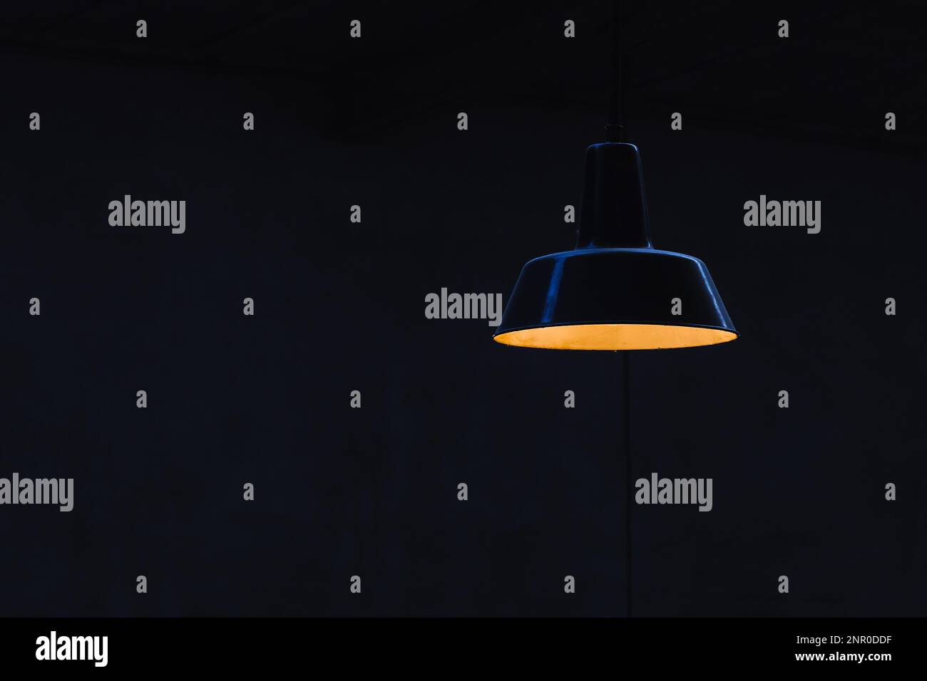 immagine con una lampada da soffitto illuminata di fronte a una parete nera Foto Stock