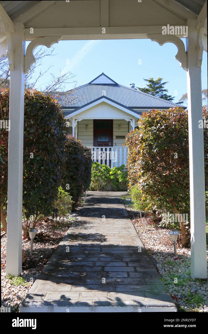 Affascinante cottage tradizionale australiano blu e bianco incorniciato da un cancello di legno bianco. Foto Stock
