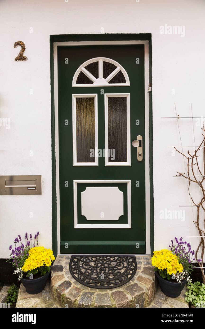 Facciata in stucco bianco con rivestimento verde e bianco porta d'ingresso in legno e fiori gialli in contenitori a fine estate, Warnemunde, Germania. Foto Stock