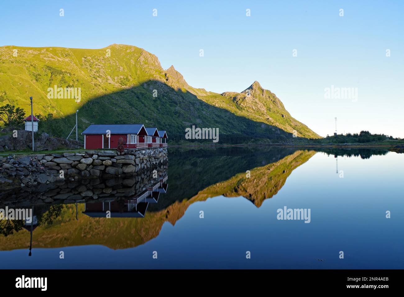 Case in legno e montagne che si riflettono nel basso fiordo d'acqua, cabine vacanze, Brustranda Sjocamping, Valberg, Lofoten, Nordland, Norvegia Foto Stock