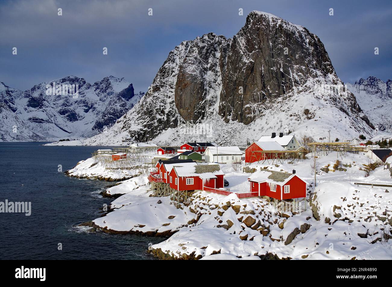 Case di legno rosso e aspre, montagne selvagge da un fiordo, inverno, vacanze, turismo, idil invernale, Hamnöy, Reinefjorden, Lofoten, Norvegia, Europa Foto Stock