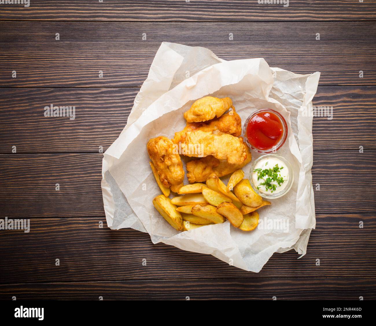 Pesce e patatine fast food tradizionali nazionali inglesi con salse assortite a scelta, su carta, rustico sfondo di legno marrone, vista dall'alto. Batteria Foto Stock