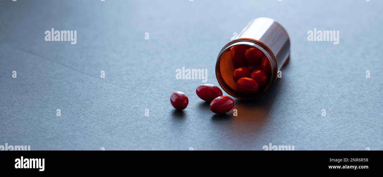 Capsule rosse e bottiglia di plastica marrone su sfondo scuro. Banner farmacia. Farmaci da prescrizione. Sanità e medicina. Industria farmaceutica. Foto Stock