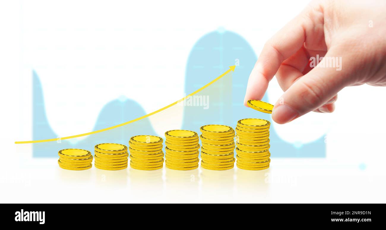 La mano sta cadendo la moneta dell'oro sulla pila delle monete con la freccia in su e il grafico di affari sullo sfondo bianco, investimento e concetto di risparmio dei soldi Foto Stock