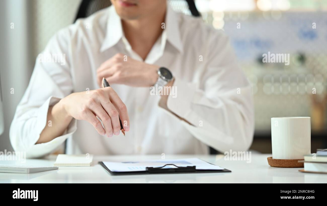Immagine ritagliata dell'analista finanziario in una maglietta bianca seduta presso la sua postazione di lavoro e analizzando i dati statistici Foto Stock
