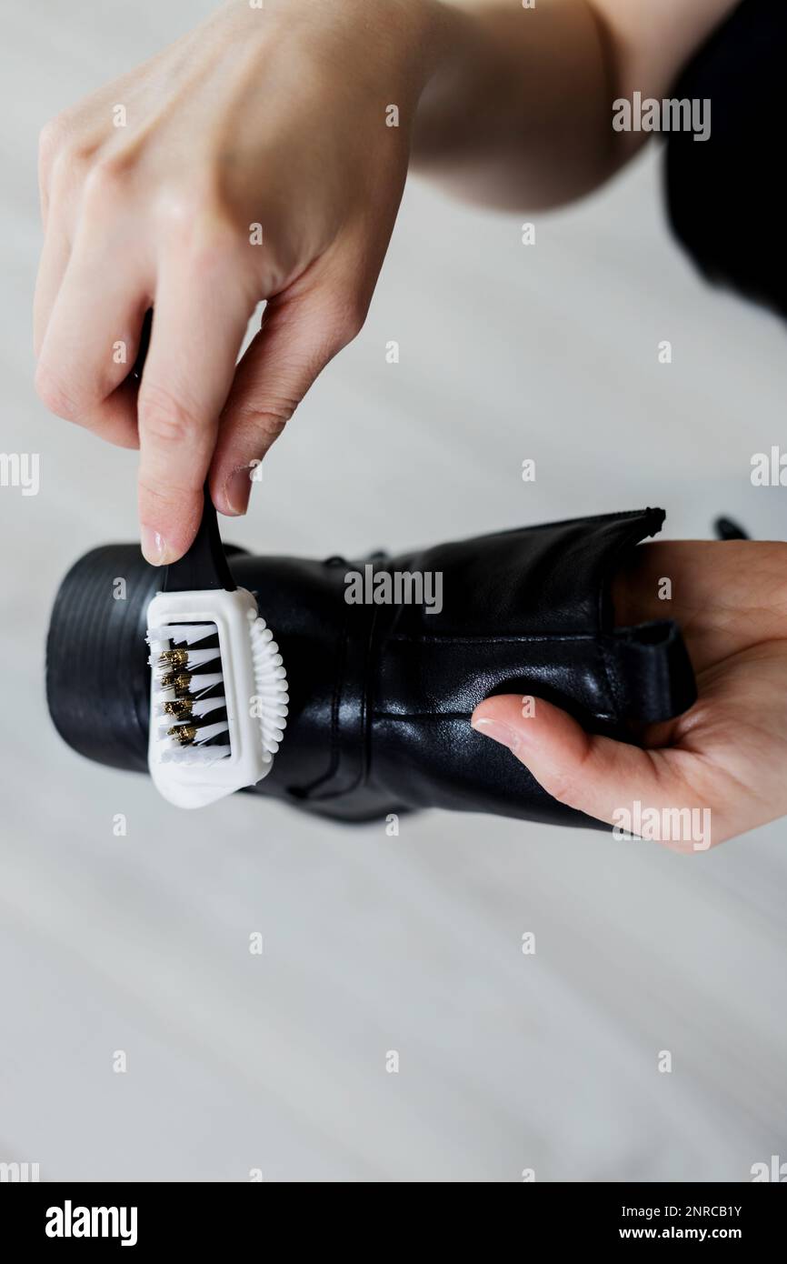 Mani che puliscono la scarpa da donna (stivale) con una spazzola. Manutenzione delle calzature Foto Stock