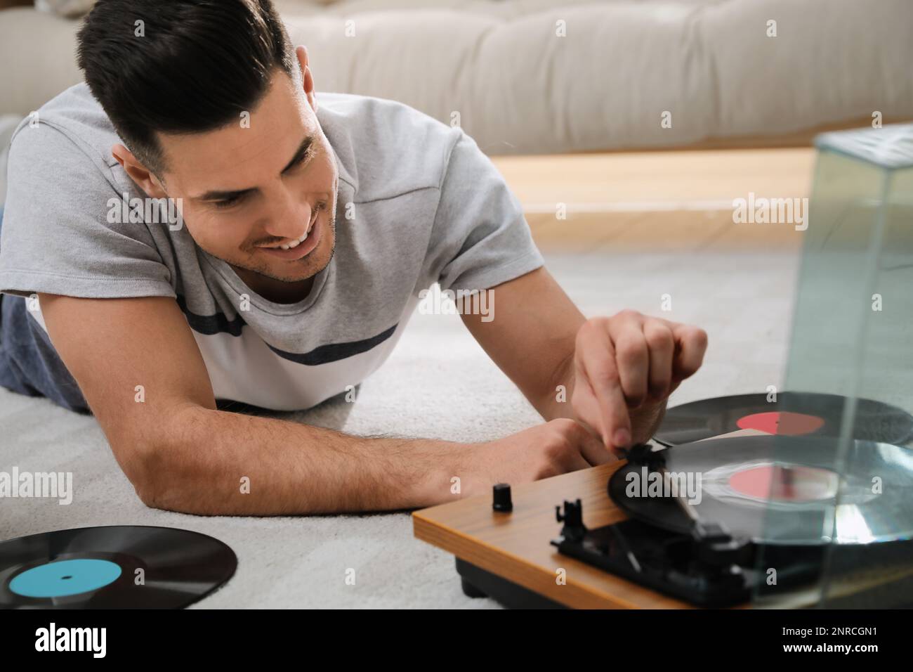 Uomo felice che usa il giradischi mentre si sdraiava sul pavimento a casa Foto Stock