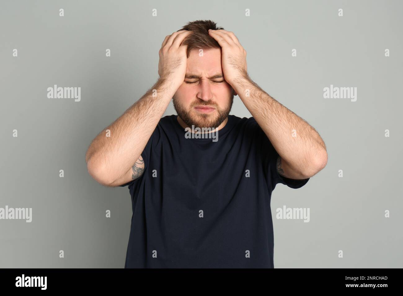 Uomo che soffre di emicrania su sfondo grigio Foto Stock