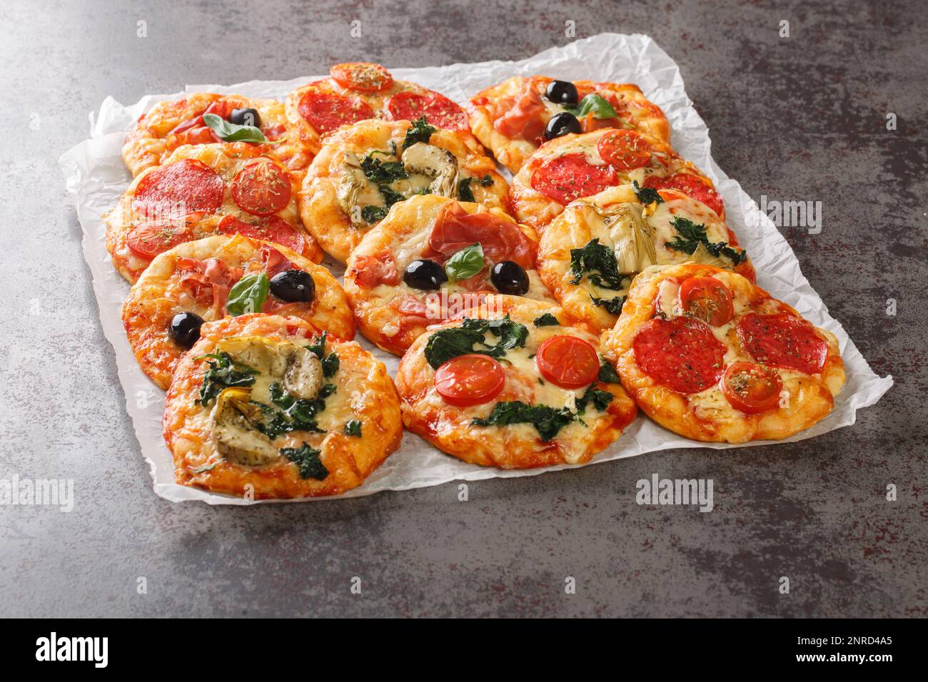 Mini pizza o pizzette assortite calde con vari condimenti primo piano su pergamena sul tavolo. orizzontale Foto Stock