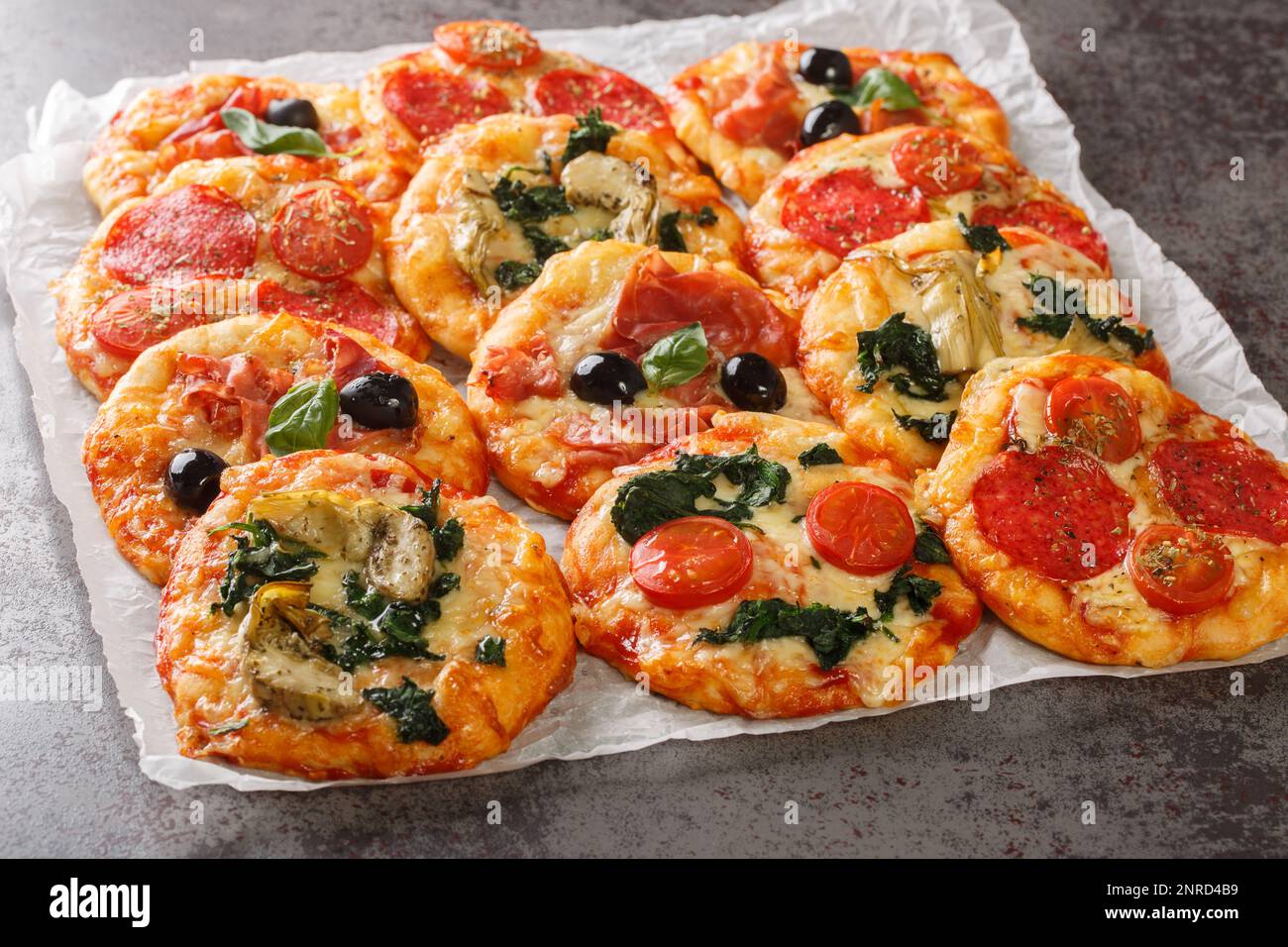 Pizza italiana Mini Pizza Bites con condimenti assortiti primo piano su pergamena sul tavolo. Orizzontale Foto Stock