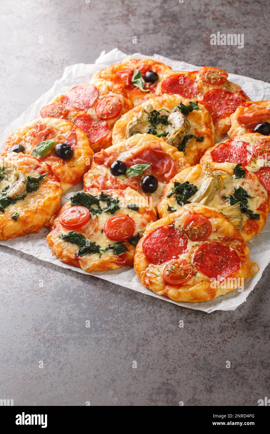 Mescolare la mini pizza o la pizzetta con vari condimenti primo piano sul pergamena sul tavolo. Verticale Foto Stock