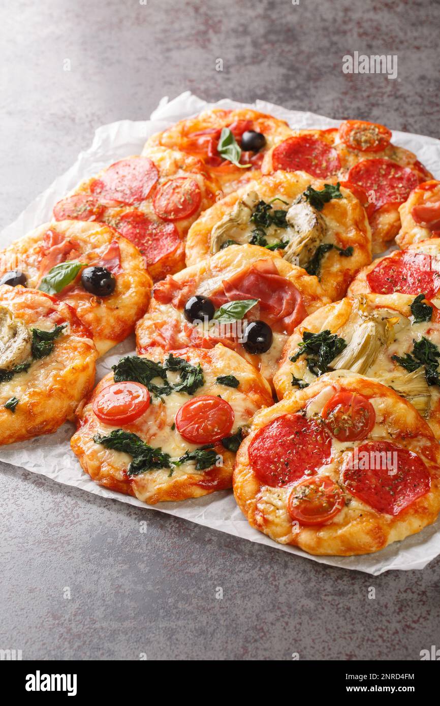 Mini pizze fatte in casa Pizzette con condimenti vegetariani e carnosi primo piano sul pergamena sul tavolo. Verticale Foto Stock