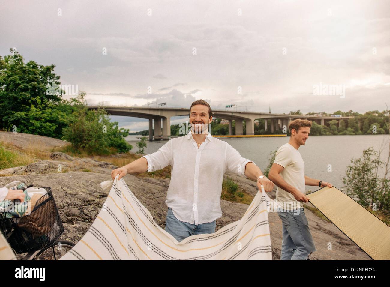 Uomo felice che posa coperta mentre si è in piedi sulla roccia durante il picnic Foto Stock