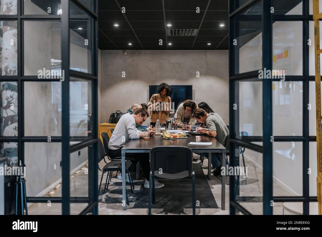 Colleghi maschi e femmine multirazziali che scrivono mentre discutono in riunione nella sala del consiglio di amministrazione Foto Stock