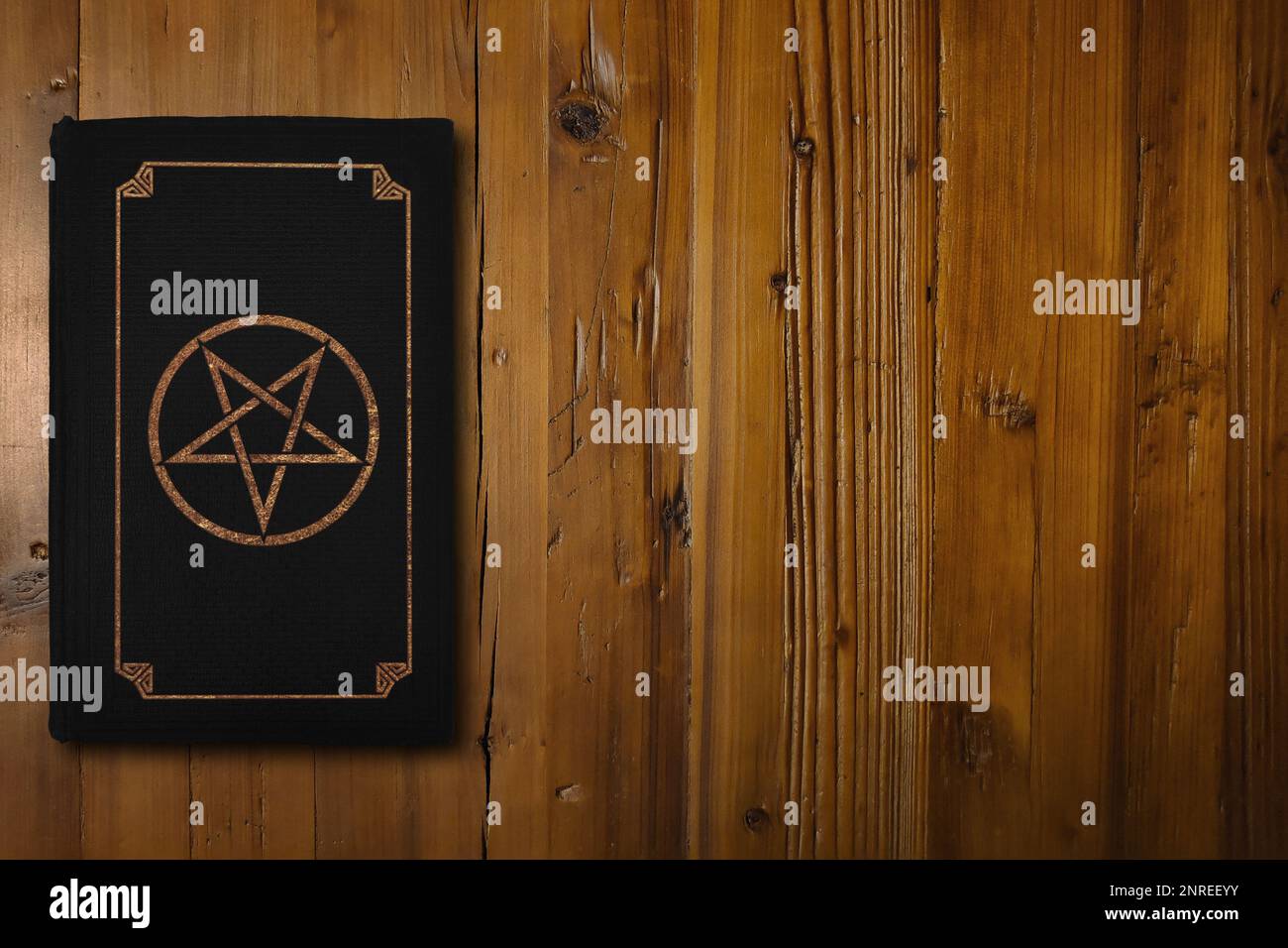 Primo piano su un libro nero con un Pentagram inverso dorato su un pannello di legno marrone. Foto Stock