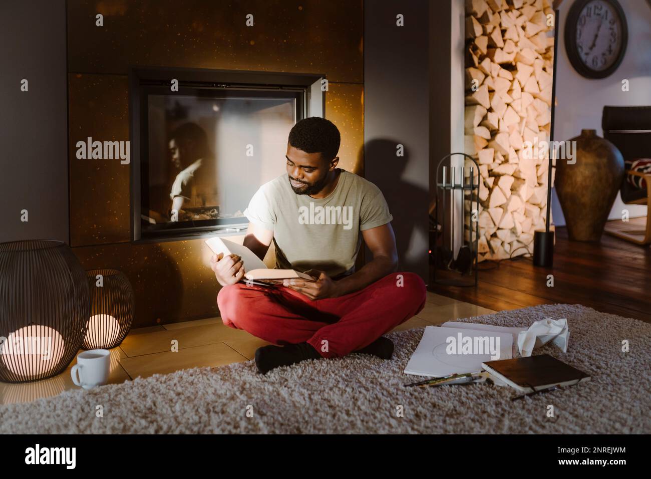 Giovane uomo che legge il libro mentre è seduto a gambe incrociate a casa Foto Stock