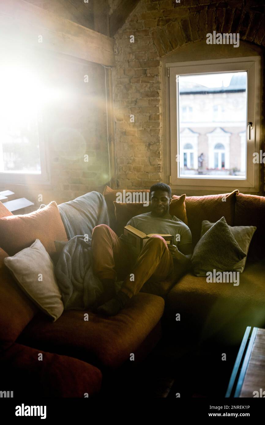 Uomo che passa il tempo libero mentre legge libro sul divano a casa Foto Stock