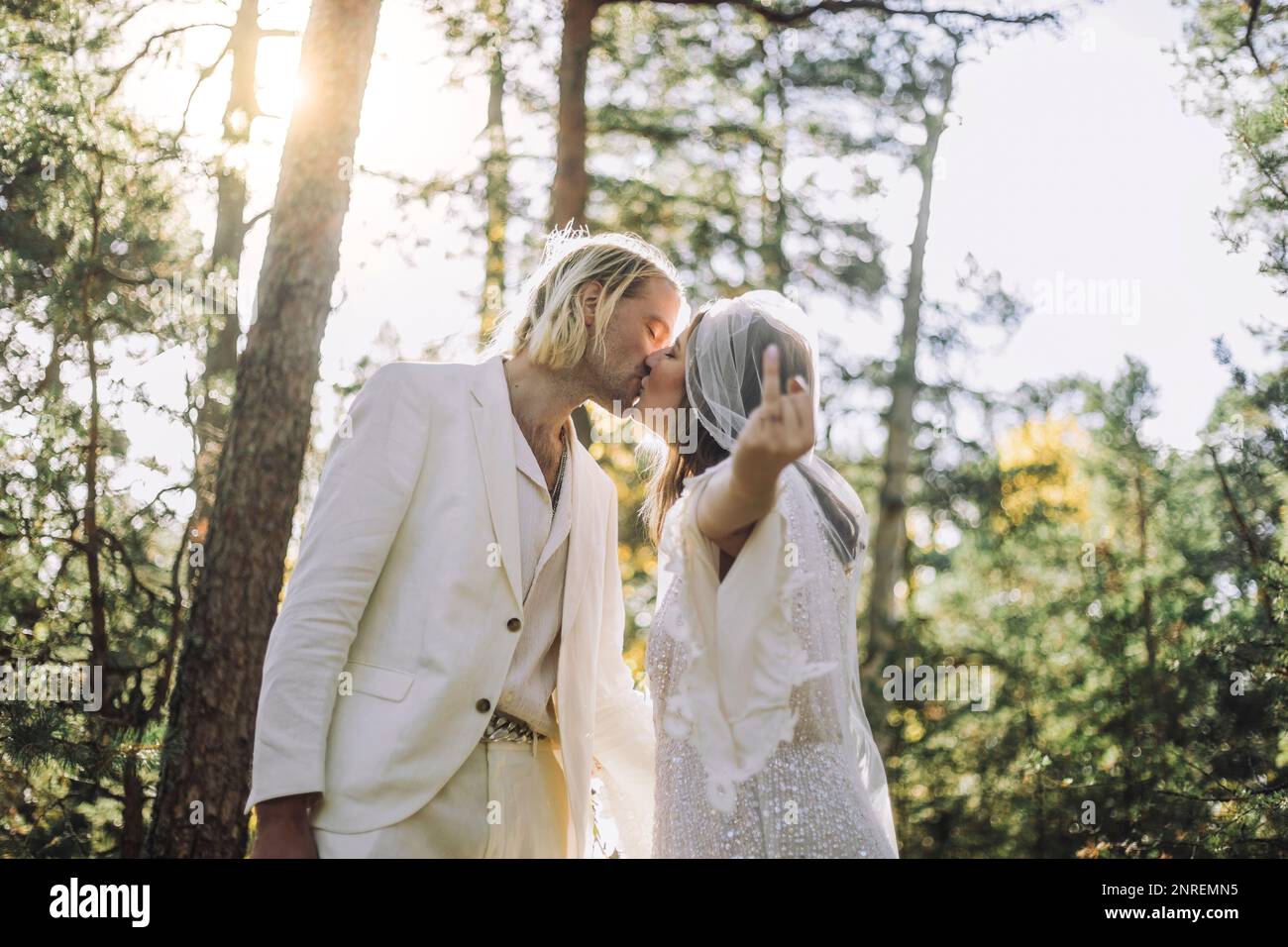 Sposa che mostra il dito anello mentre bacia lo sposo sulla bocca nella foresta durante il matrimonio Foto Stock