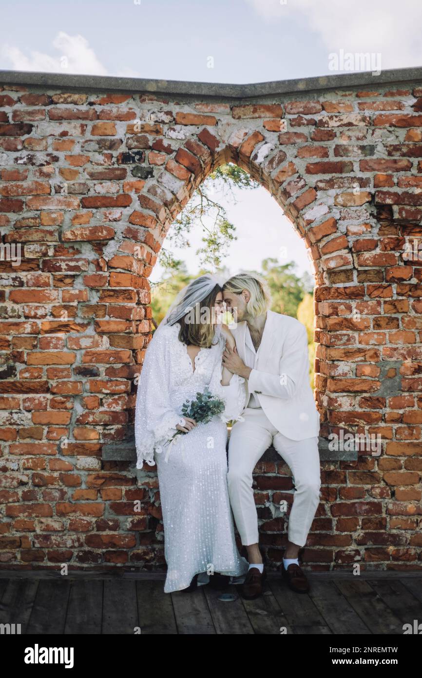 Sposo sorridente e sposa seduto faccia a faccia sul davanzale della finestra durante il matrimonio Foto Stock