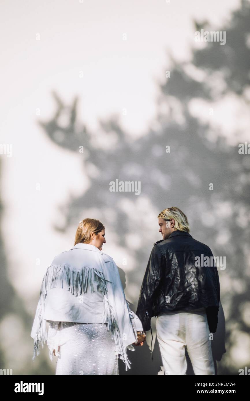 Vista posteriore della sposa e dello sposo appena sposati che tengono le mani mentre si guardano l'un l'altro il giorno del matrimonio Foto Stock