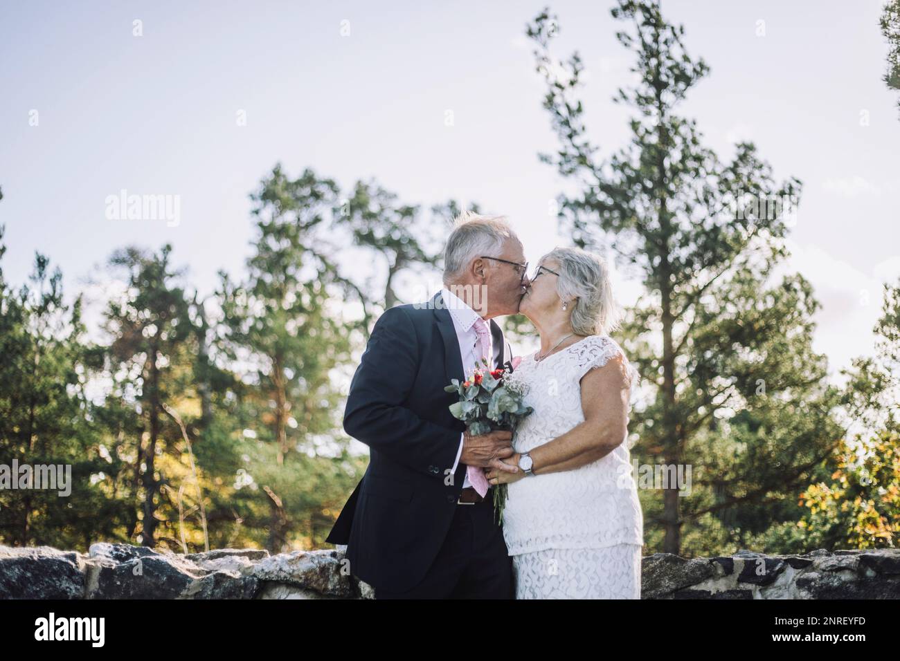 Coppia anziana sposata affettuosa baciata in bocca contro la foresta il giorno del matrimonio Foto Stock