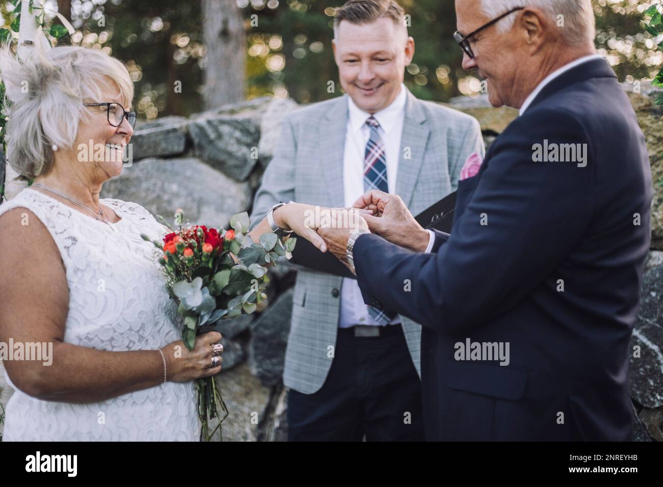 Sposo superiore che mette l'anello di nozze nel dito della sposa dal ministro durante la cerimonia Foto Stock
