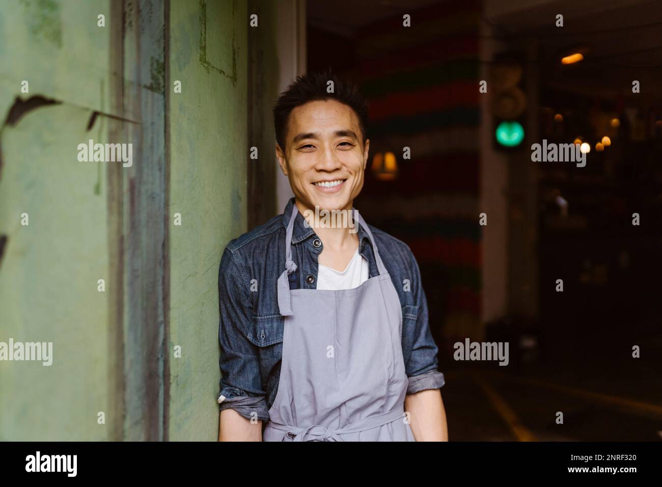 Ritratto del proprietario sorridente del ristorante in grembiule appoggiato al muro Foto Stock