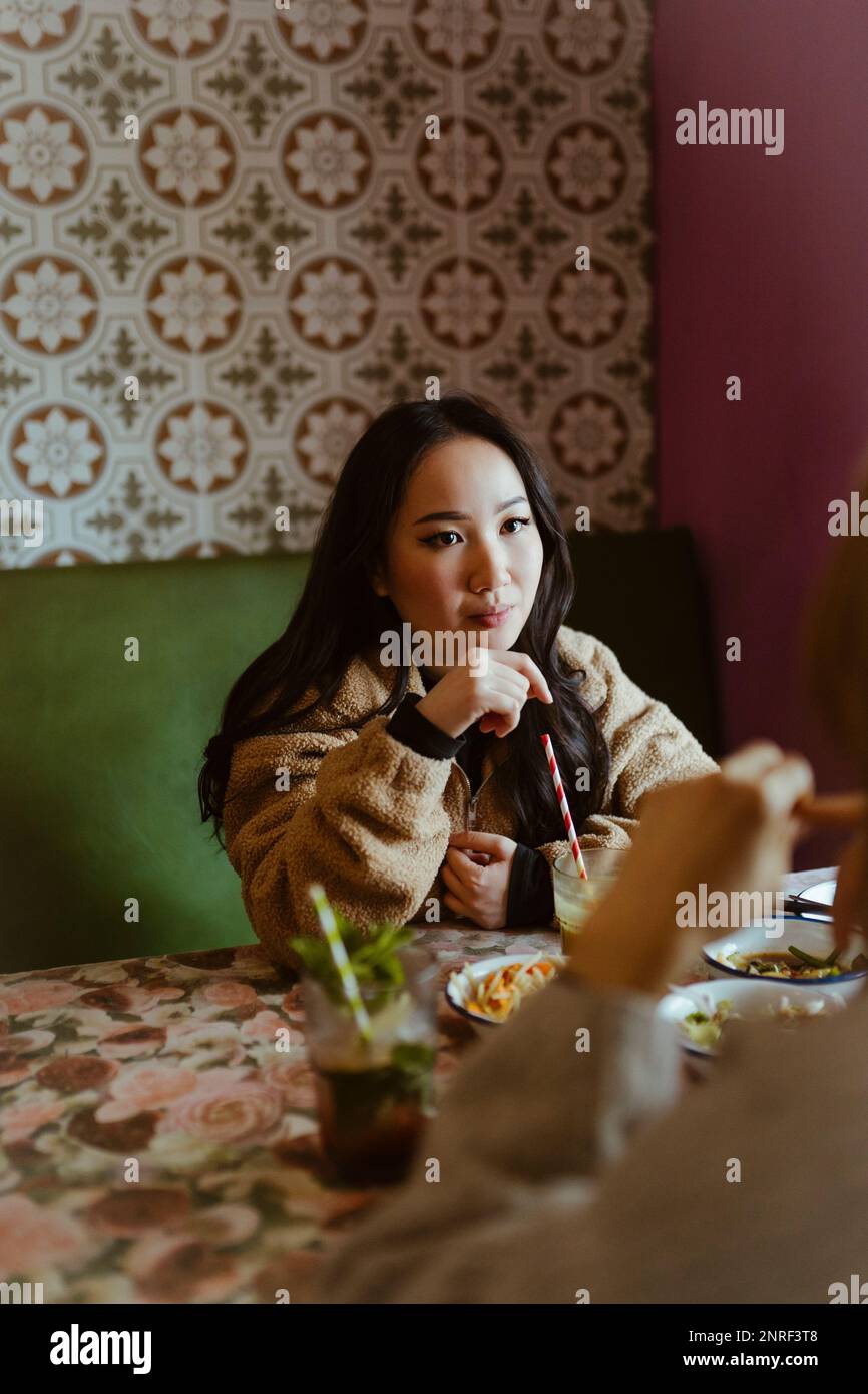 Giovane donna che parla con un amico durante il pranzo al ristorante Foto Stock