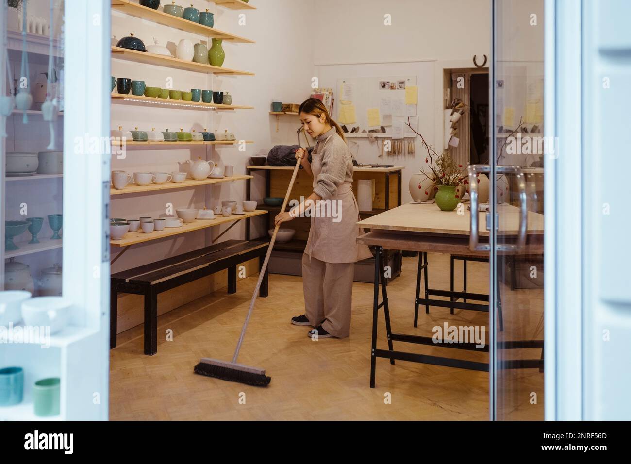 Vasaio femmina per la pulizia del pavimento con scopa in piedi in officina Foto Stock