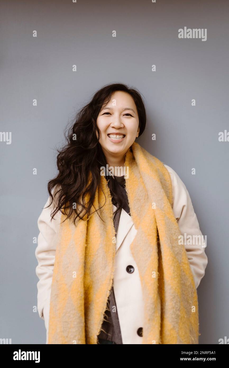 Ritratto di donna felice che indossa abiti caldi mentre si trova su sfondo grigio Foto Stock