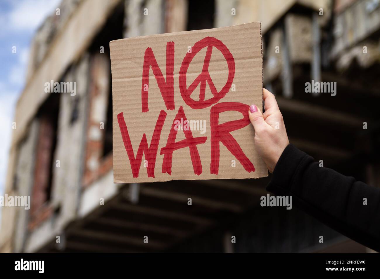 Donna con cartello No War con segno di pace in protesta contro la guerra. Dimostrazione in edificio rovinato, bombardato, distrutto. Donna con banner anti-guerra. Foto Stock