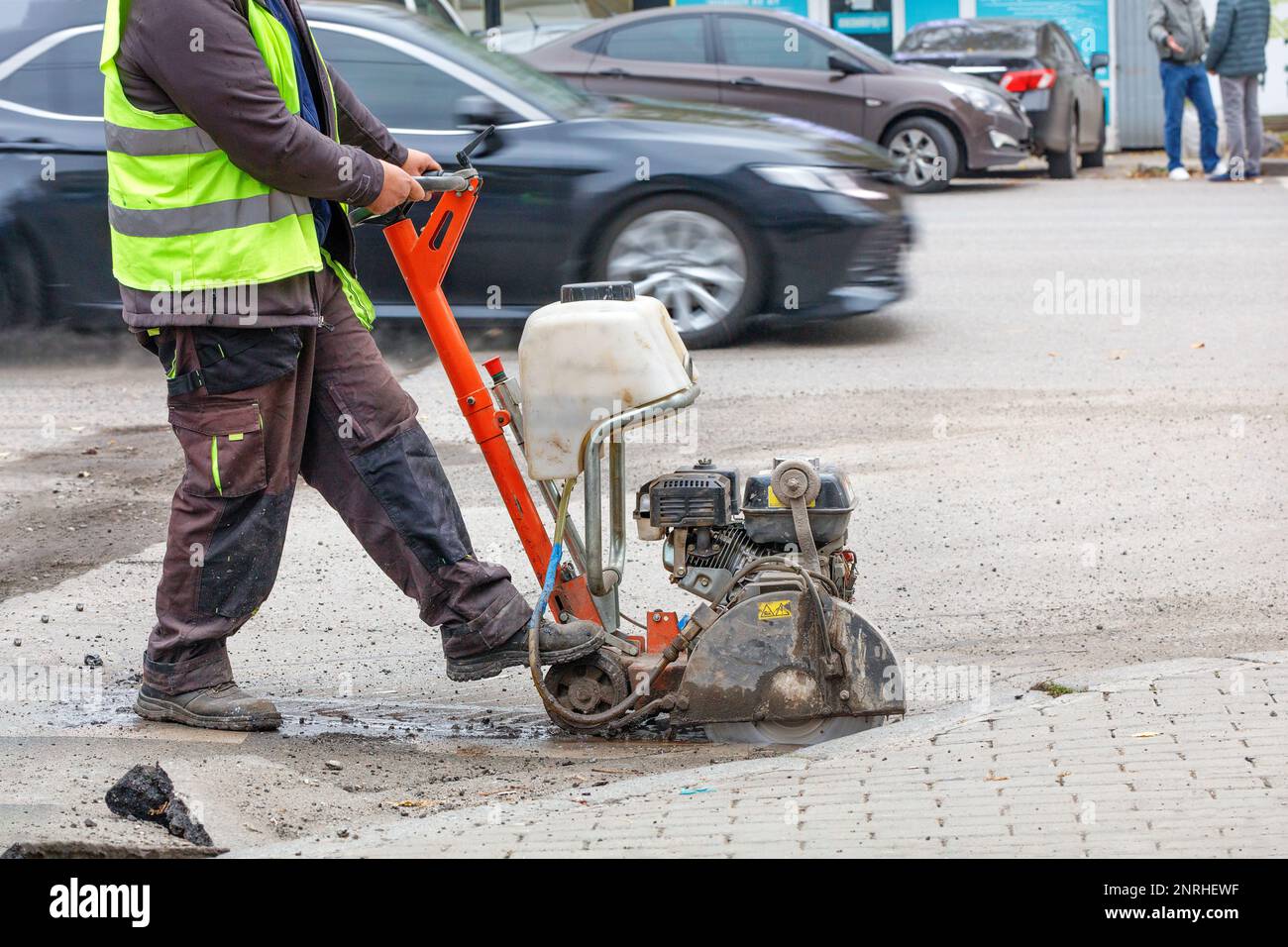 Un lavoratore della strada sta riparando la carreggiata di una strada cittadina, tagliando una sezione difettosa con una fresa a benzina con una lama diamantata. Spazio di copia. Foto Stock