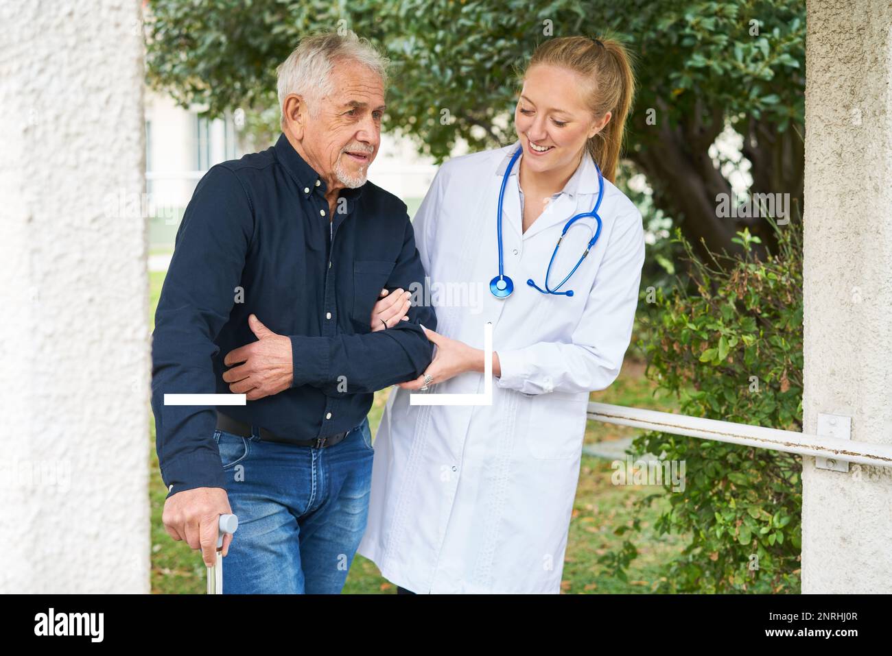Giovane donna sorridente che assiste l'uomo anziano disabile a camminare in giardino Foto Stock