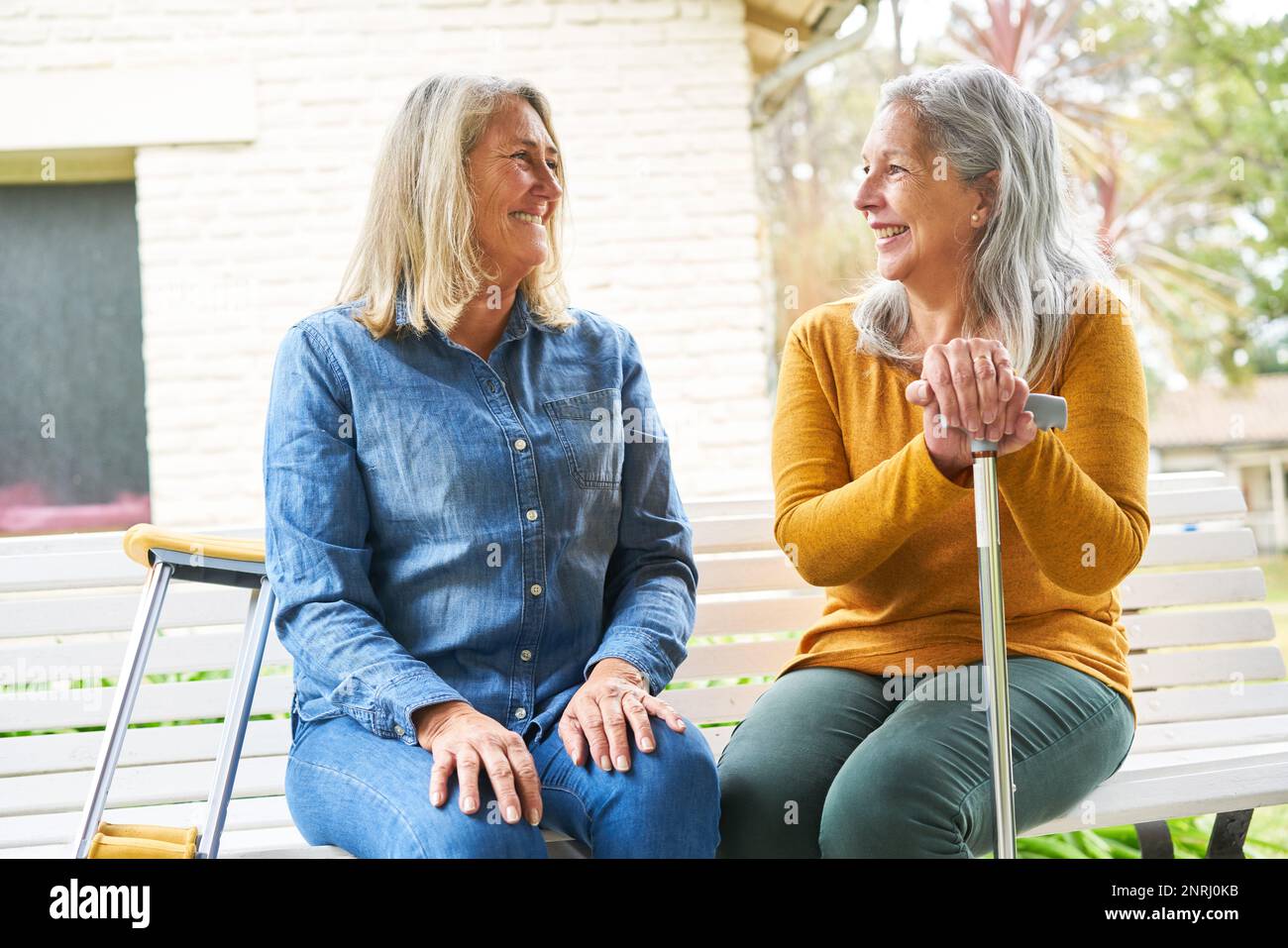 Donna anziana felice che discute con l'amico femmina seduto sulla panca in giardino Foto Stock