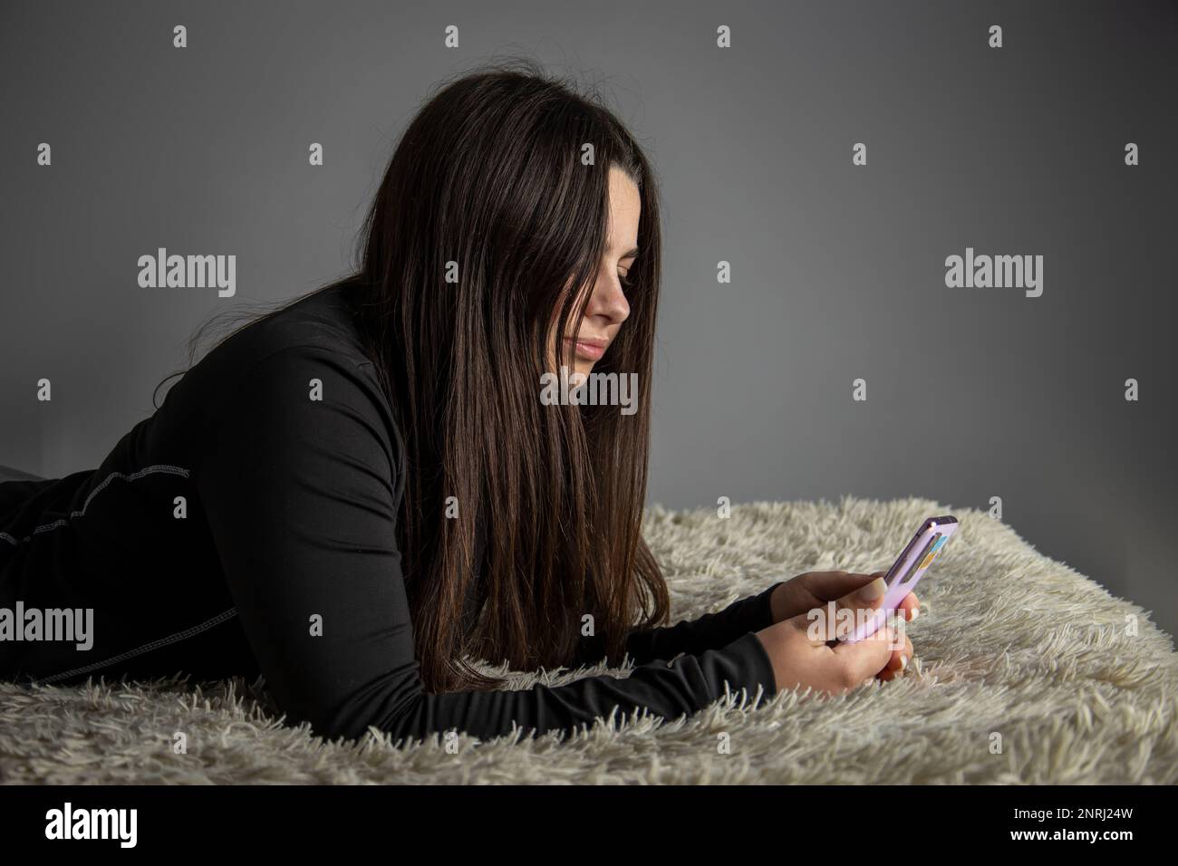Una bella ragazza è sdraiata sul letto con un telefono cellulare. Foto Stock