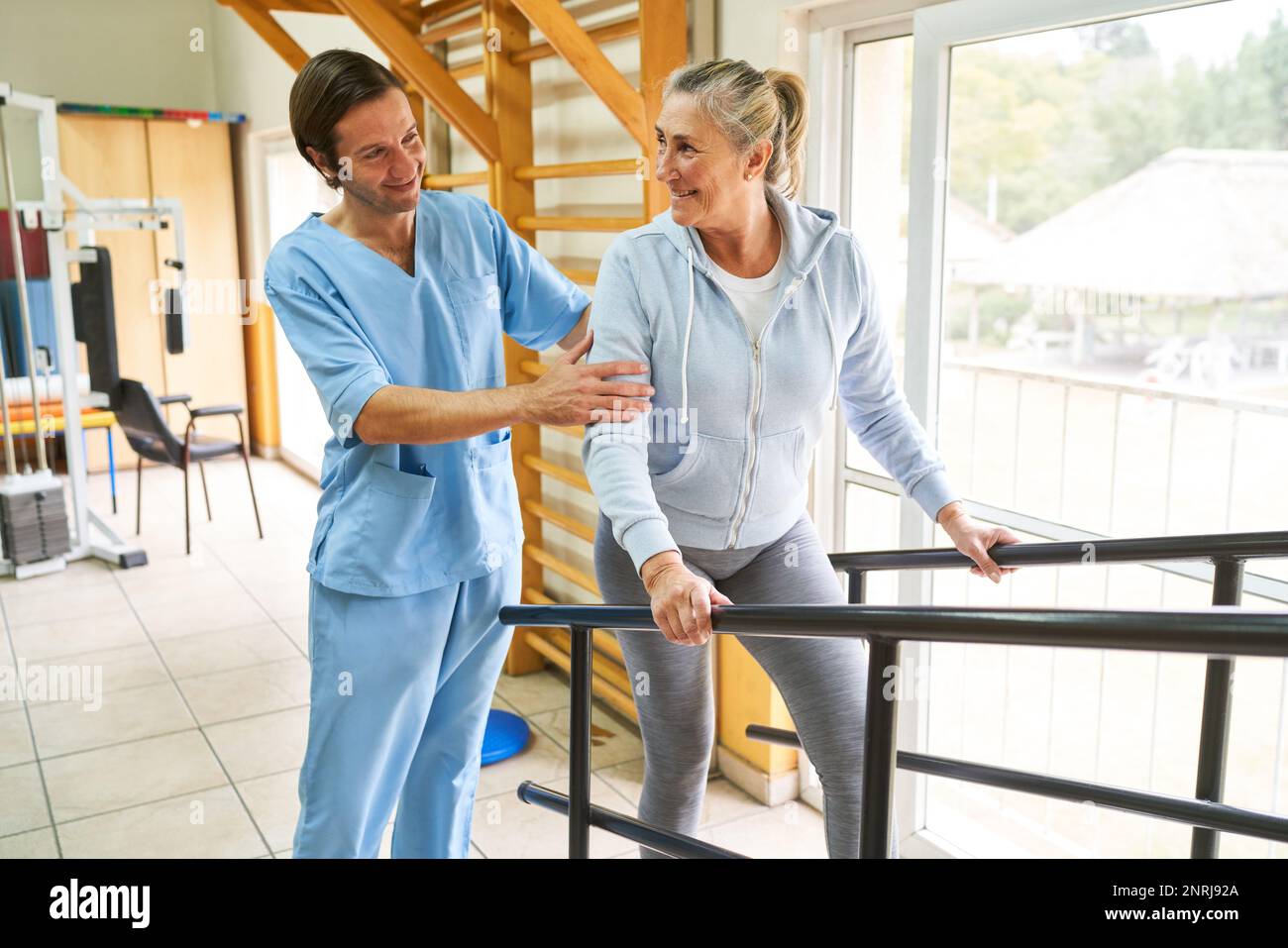 Fisioterapista maschile sorridente che assiste una donna anziana nella terapia del movimento presso il centro di riabilitazione Foto Stock