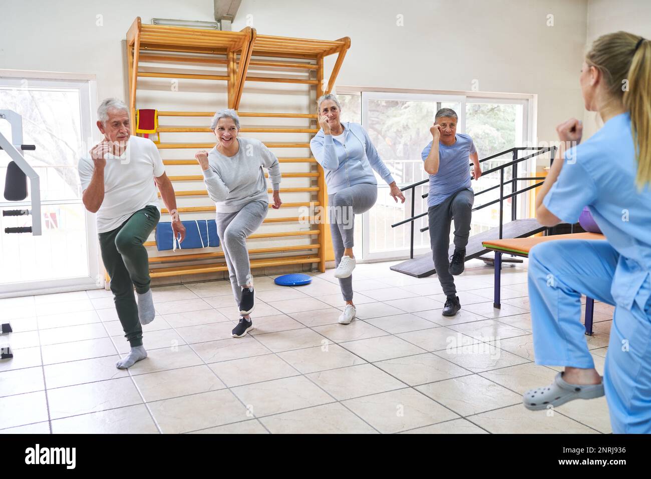 Gruppo di persone anziane che ballano e si allenano in classe di fitness di casa di cura con caregiver femminile Foto Stock