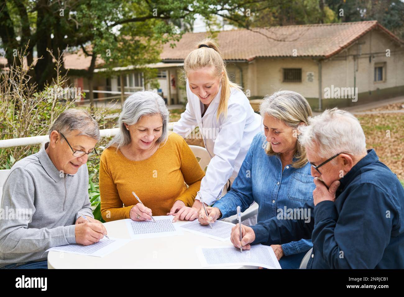 Dottore con gruppo di amici anziani risolvere puzzle cruciverba e labirinto sul tavolo in giardino di casa di cura Foto Stock