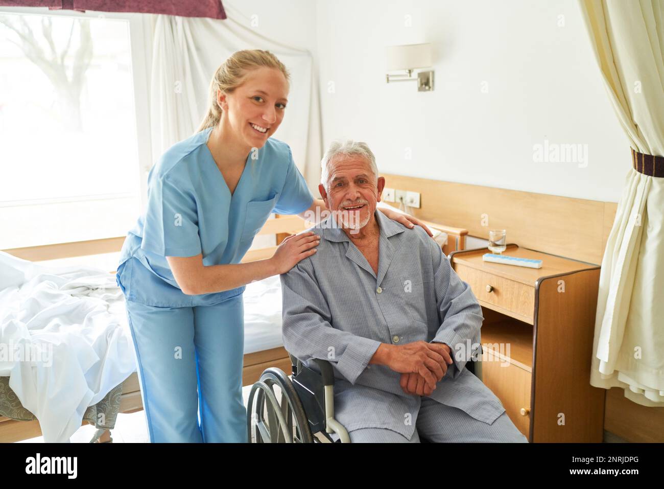 Ritratto di un caregiver sorridente con un anziano seduto in sedia a rotelle al centro di riabilitazione Foto Stock