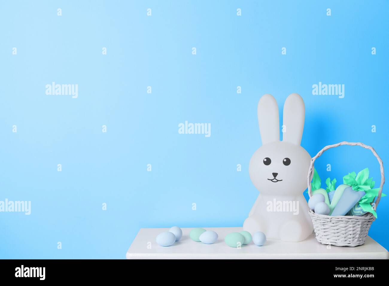 Coniglio di Pasqua giocattolo bianco, cestino con carote giocattolo e uova di Pasqua su sfondo blu Foto Stock
