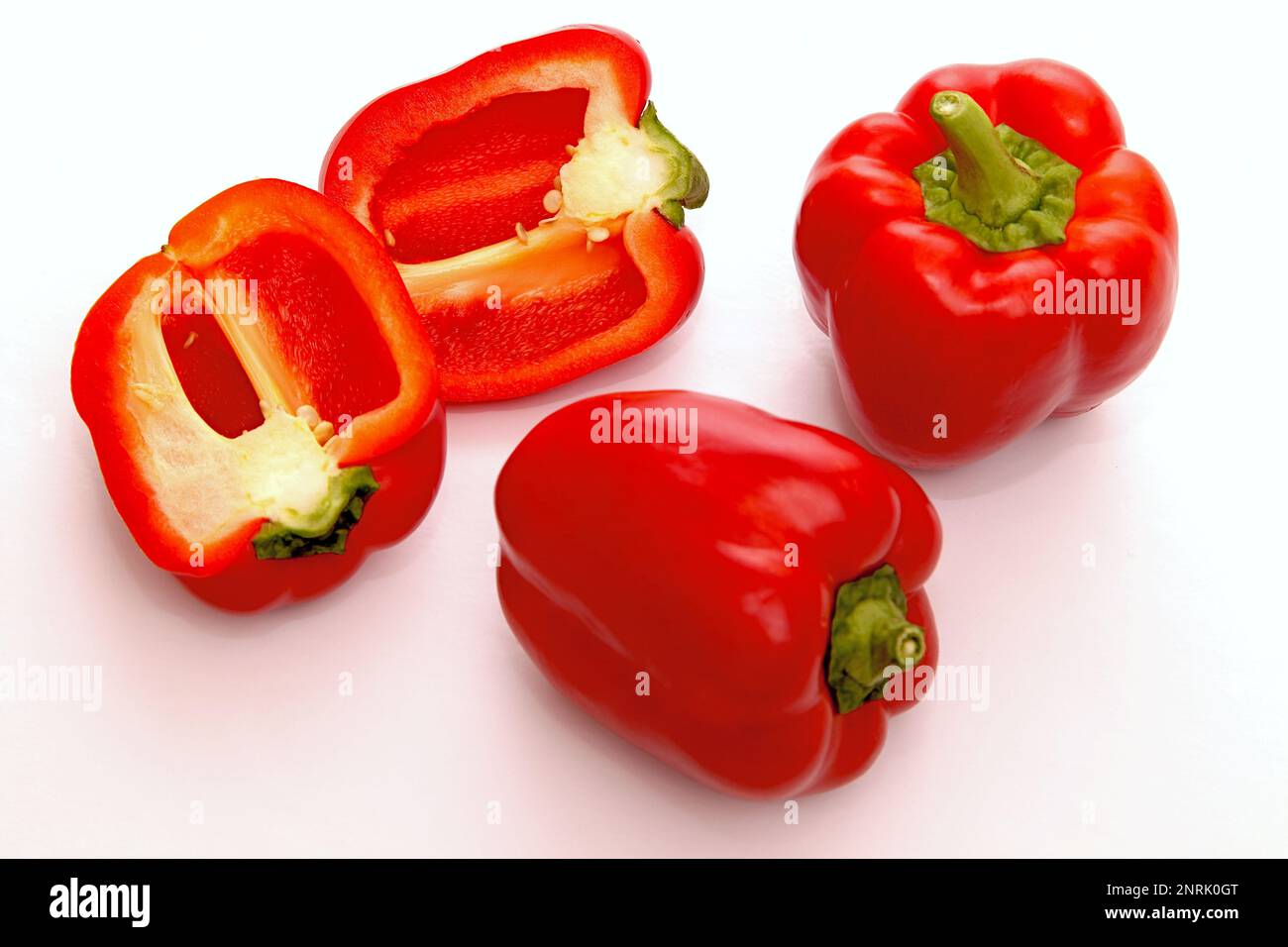 Un peperone rosso accanto a due metà tagliate e un pezzo Foto Stock