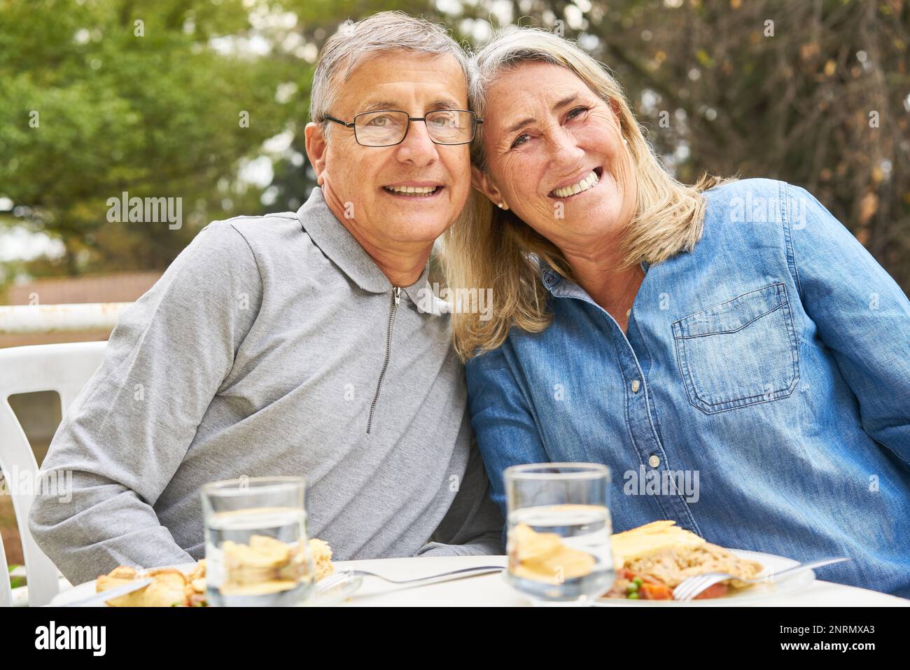 Ritratto di felice uomo anziano e donna seduto con pasto a tavola nel giardino di casa di cura Foto Stock