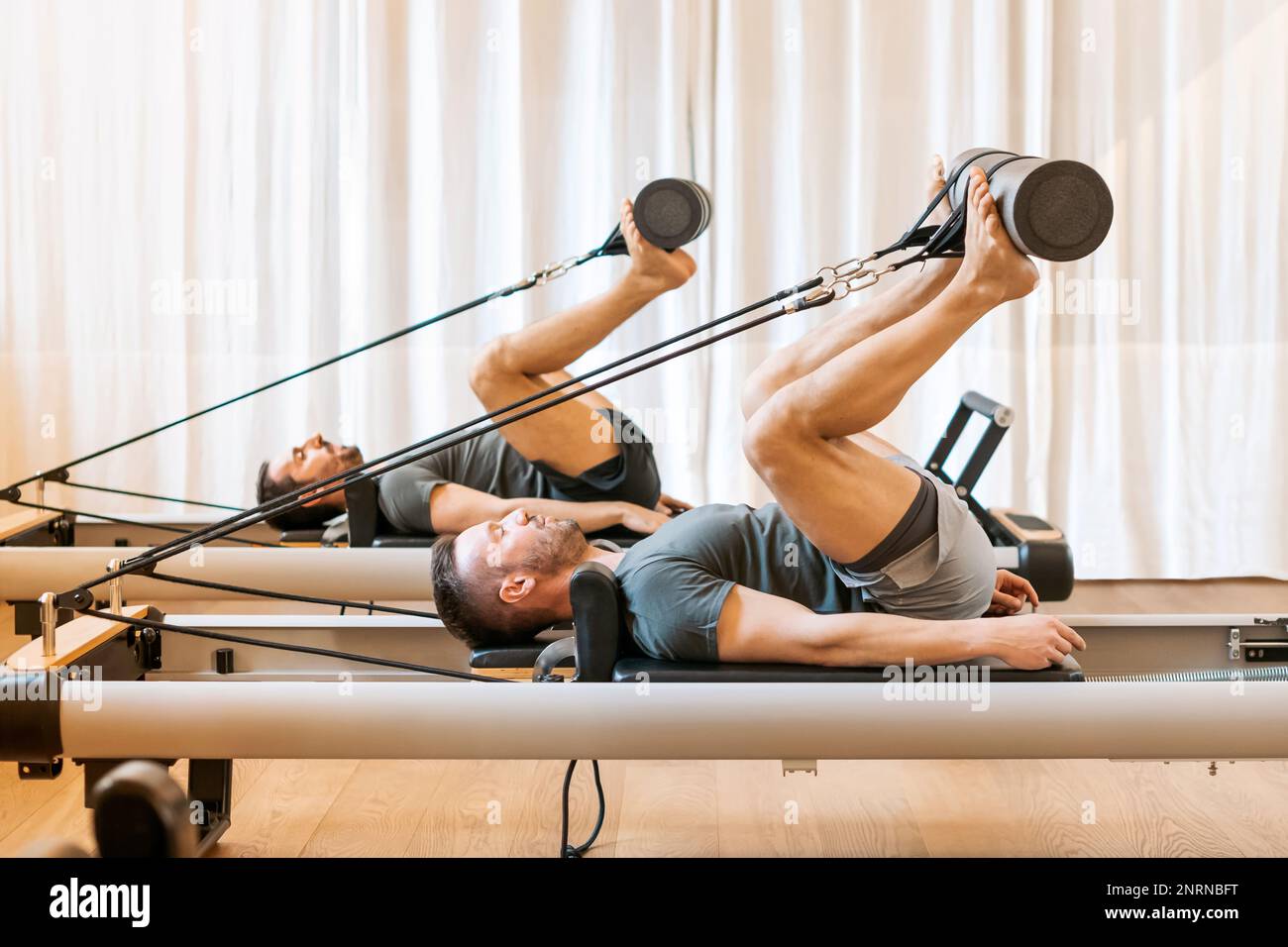 Vista laterale di atleti maschi concentrati in abbigliamento sportivo che si esibiscono pilates hip mobility esercizio sul reforming durante l'allenamento Foto Stock