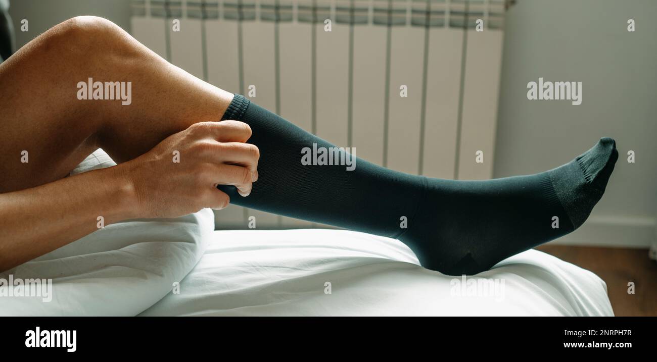 un uomo mette su un calza nera di compressione seduta sul suo letto a casa, in un formato panoramico da utilizzare come banner web o header Foto Stock