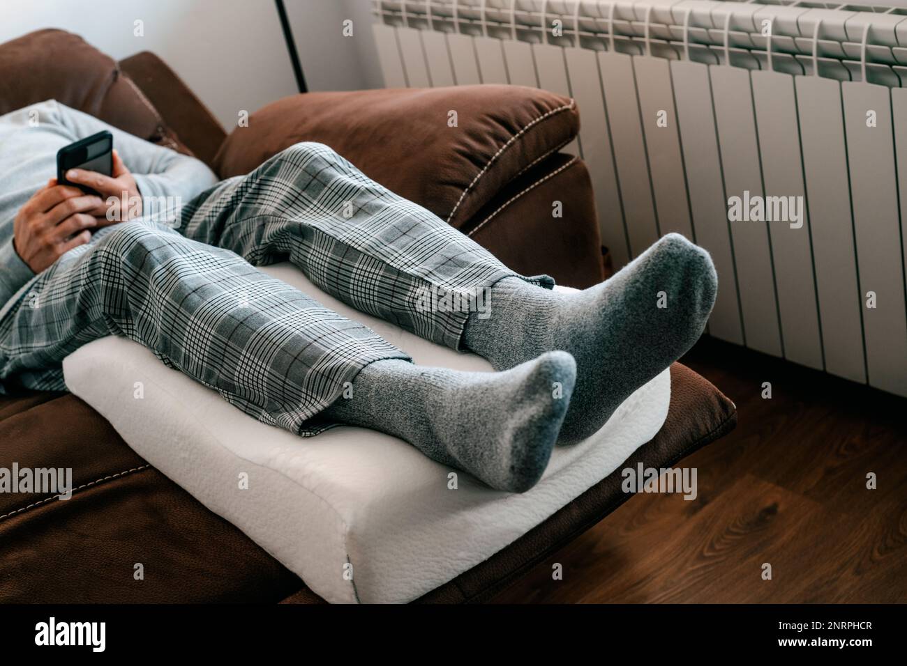 un uomo appoggia le gambe su un cuscino ad elevazione delle gambe, in schiuma di memoria, mentre si appoggia sul divano Foto Stock