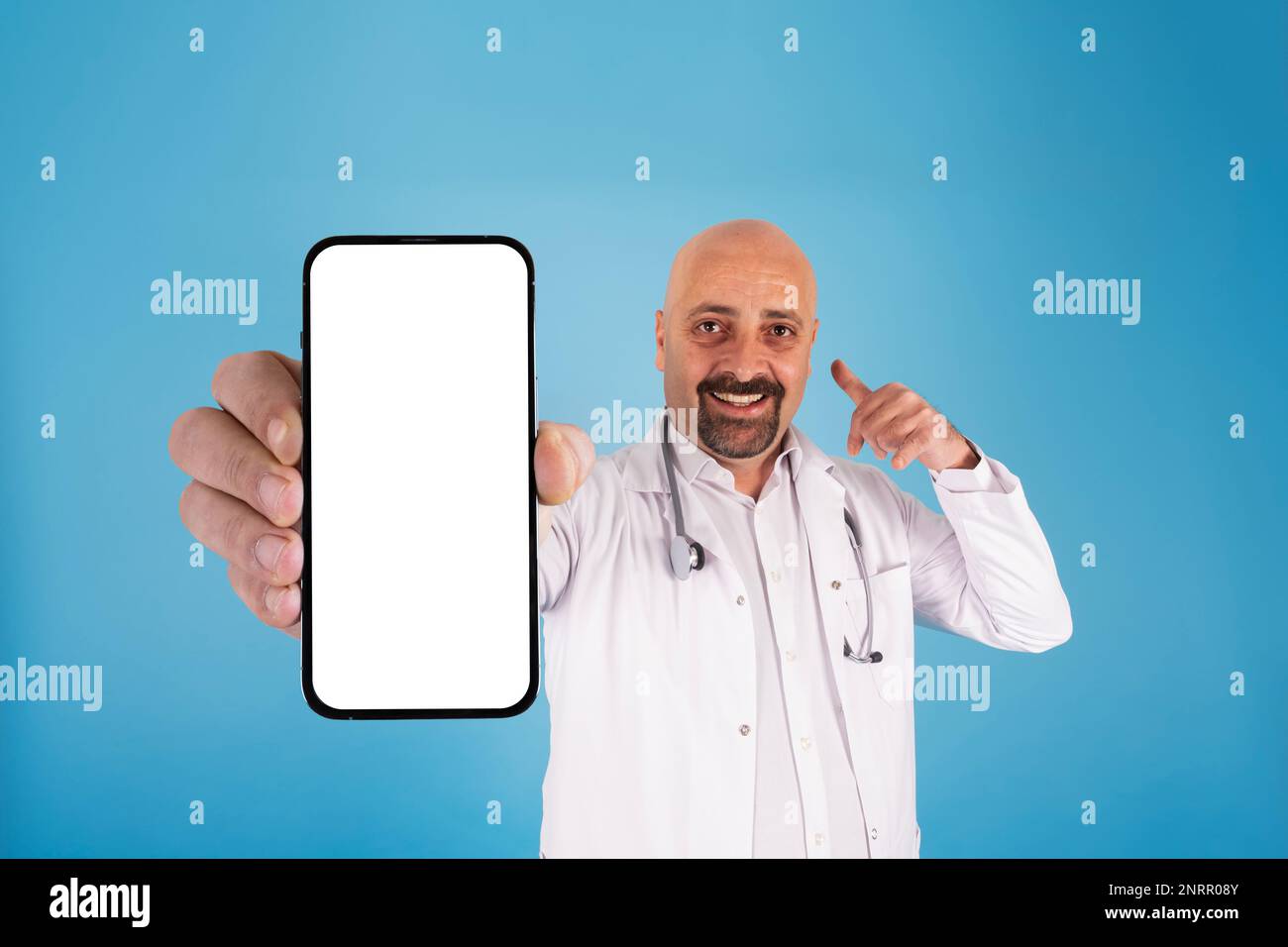 Medico che mostra lo smartphone. Gesturing mi chiamano, in posa, isolato su sfondo blu studio. Schermo vuoto del telefono cellulare per la simulazione. Foto Stock