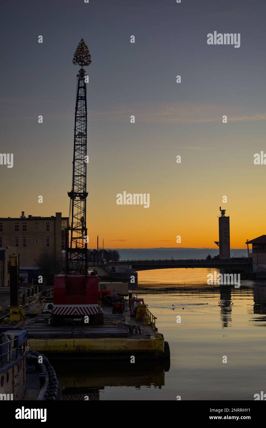 Alba e un albero di Natale in cima a un braccio di gru sul fiume a Manitowoc, Wisconsin. Foto Stock