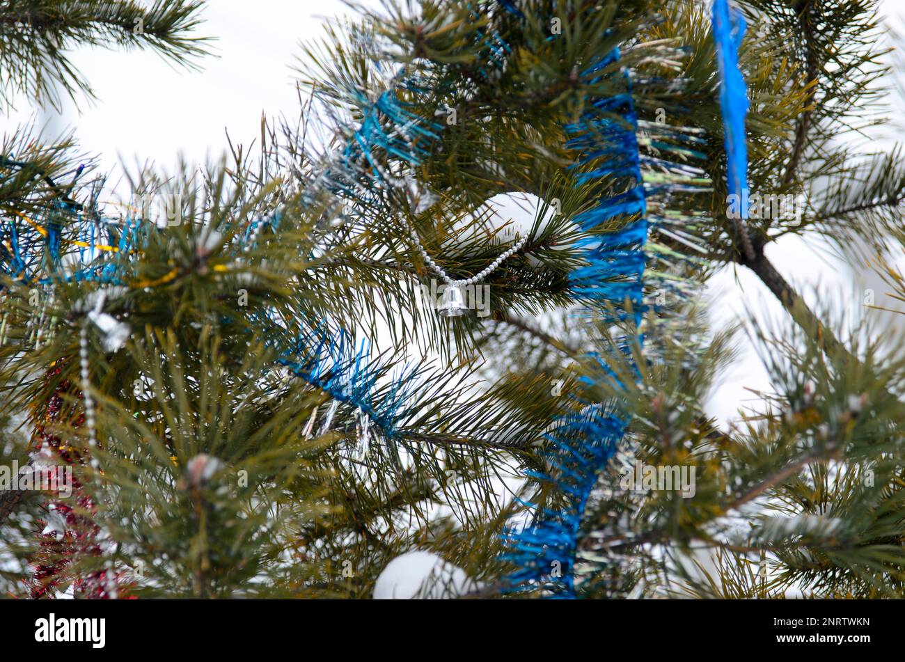 Le ghirlande multicolore e il tinsel della palla decorano l'albero di Natale all'aperto nella neve a Capodanno. Foto Stock