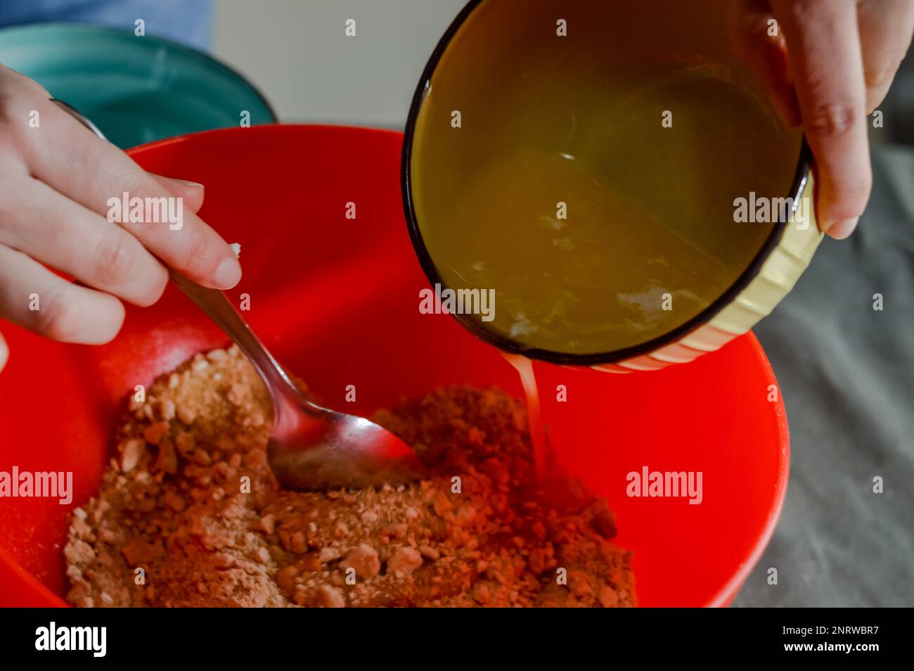 le mani versano il burro fuso in una ciotola con biscotti sbriciolati e zucchero per fare la base di una cheesecake Foto Stock
