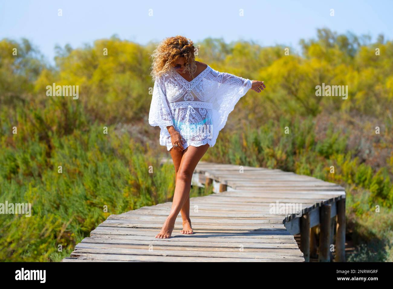 Una bella donna godere vacanze estive e destinazione di viaggio in piedi su un molo di legno con bianco elegante abito da spiaggia e bionda cu Foto Stock